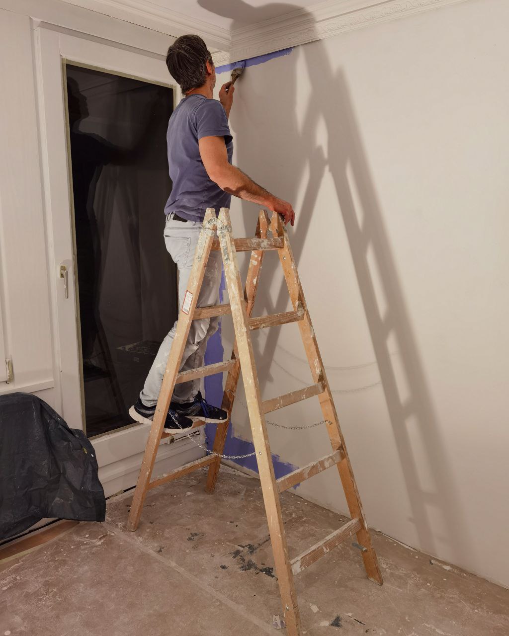 Mann steht auf einer Leiter und streicht die Wände blau